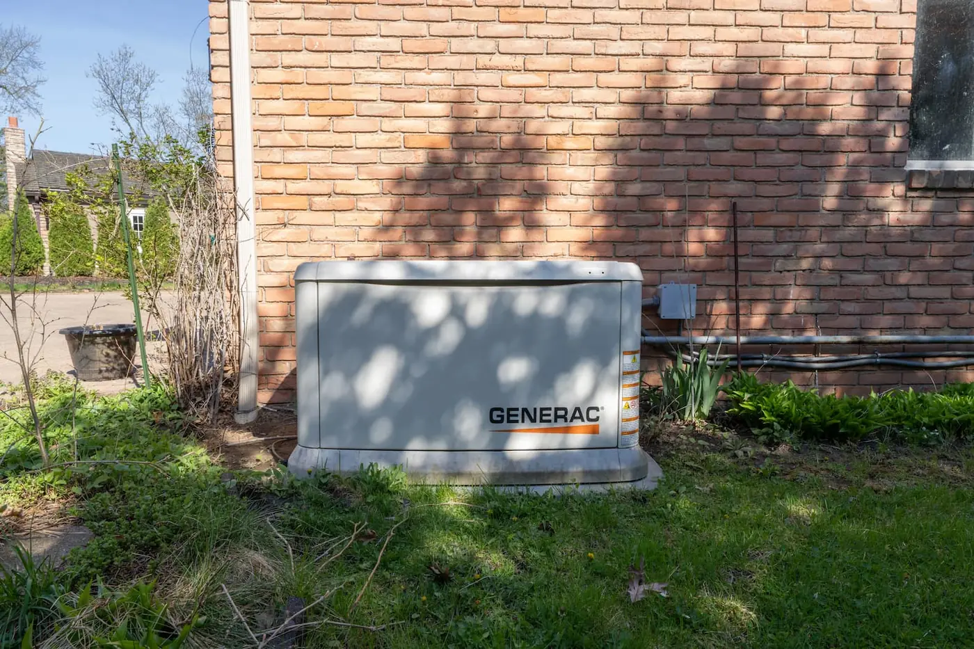 A Generac standby generator installed beside an established brick home.