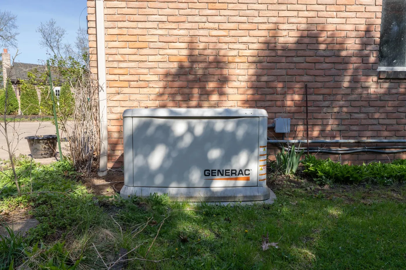 A Generac standby generator set level on a composite pad at code clearances beside a brick Fishers home.